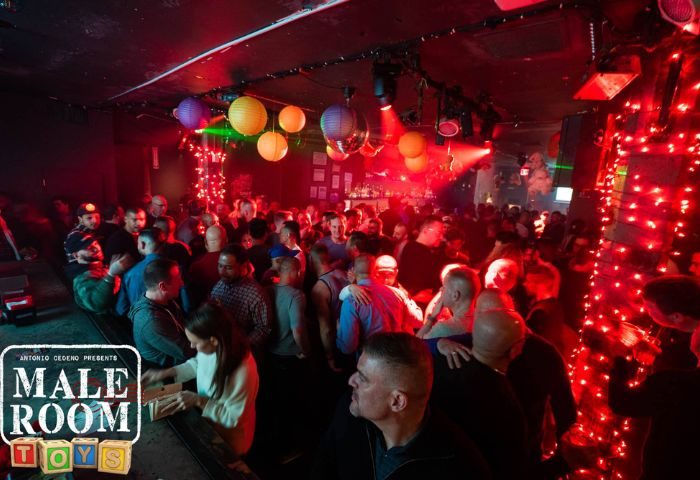 Rebar Chelsea in New York: Gay bar scene with a crowd of men, red lighting, and colorful lanterns. A popular gay travel destination.