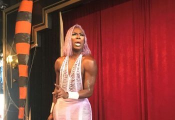 Redline Drag: A drag queen with pink hair and a pink dress points at the camera. Gay travel advice and nightlife for gay men.