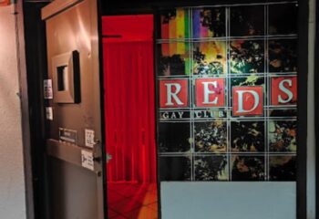 Reds Cruising Club entrance, a gay club in Gran Canaria. Red curtains and a sign reading REDS GAY CLUB are visible at the entrance.