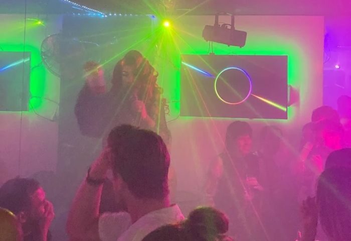Madrid gay bar Reina Pop interior. A drag queen performs amid a crowd, bathed in colorful lights and smoke. Nightlife scene.