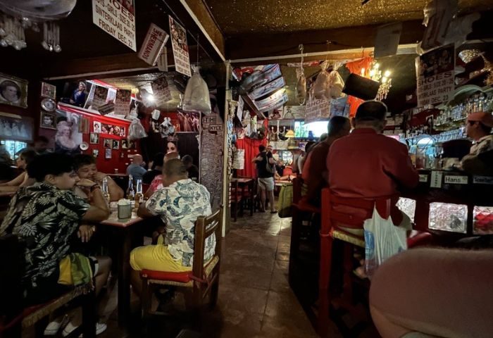 Reinas Bar, a gay-friendly place in Puerto Vallarta. People sit at tables and at the bar in a cozy, dimly lit space with eclectic decor.