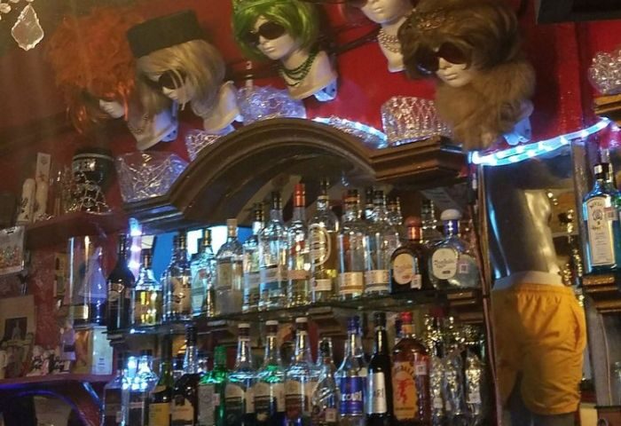 Reinas Bar, a gay place in Puerto Vallarta, Mexico. Backlit bar with liquor bottles and mannequin heads wearing wigs and sunglasses.