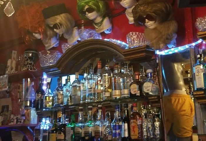 Reinas Bar, a gay place in Puerto Vallarta, Mexico. Backlit bar with liquor bottles and mannequin heads wearing wigs and sunglasses.