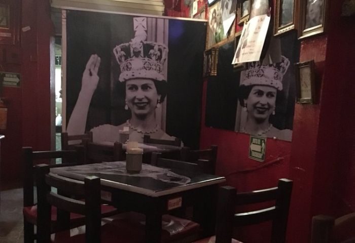 Interior of Reinas Bar, a gay place in Puerto Vallarta, featuring Queen Elizabeth II portraits on red walls, and a table with chairs.