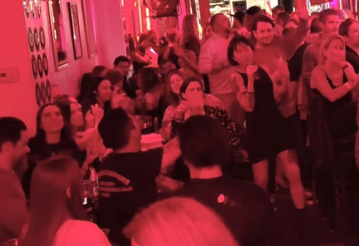 Crowded RetroRoom Lounge location. People are standing, dancing, and enjoying themselves in a gay bar with red lighting.
