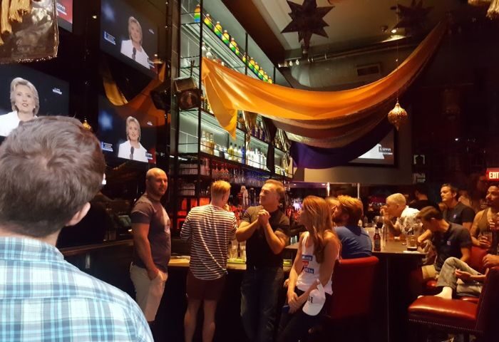 Revolver dancefloor scene at a gay bar. People are gathered, watching TV screens. Travel advice for gay men seeking nightlife.