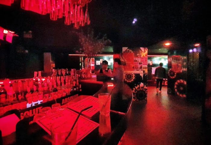 Shanghai gay bar interior. Red lighting, bar with drinks, bartenders, and patrons. Nightlife and travel for gay men in Shanghai.
