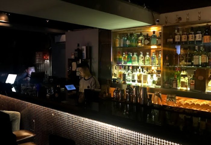 Rice Bar in Shanghai: Bartender stands behind the bar with liquor bottles on shelves. Gay travel advice for nightlife in China.