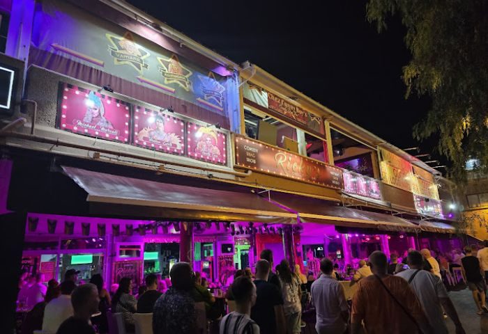 Ricky's Cabaret Bar, a gay bar in Gran Canaria, at night. Crowds gather outside the colorful, illuminated venue for entertainment.