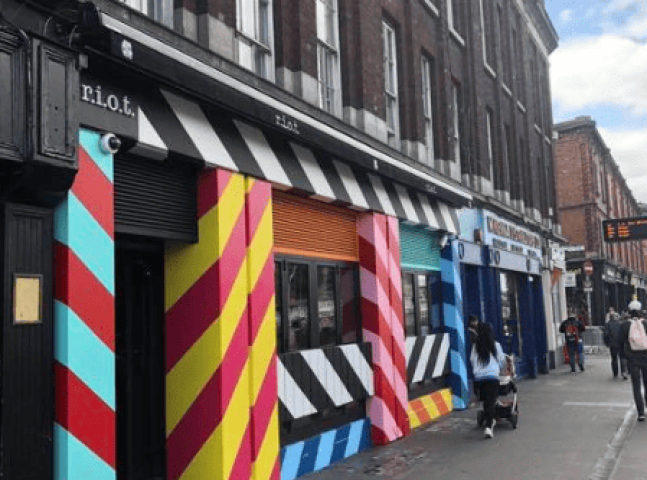 Dublin's Riot Gay Bar exterior. Colorful striped facade with black and white awning. A vibrant spot for gay men's travel in Ireland.
