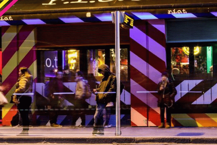 Riot Gay Bar, Dublin. Night scene with people outside the bar, which has a red and white striped facade. Gay travel advice.