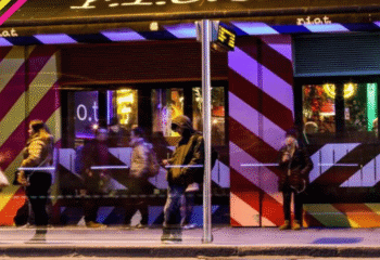 Riot Gay Bar, Dublin. Night scene with people outside the bar, which has a red and white striped facade. Gay travel advice.