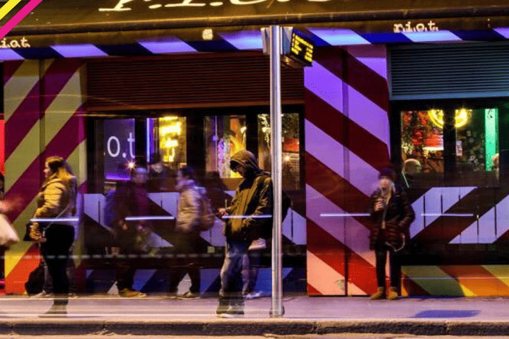 Riot Gay Bar, Dublin. Night scene with people outside the bar, which has a red and white striped facade. Gay travel advice.