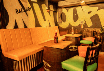 Riot Gay Bar Dublin interior. Cozy seating area with orange bench, barrel tables, and colorful chairs. Graffiti art on the walls. Gay travel.