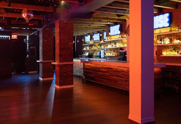 Interior of Rise Gay Bar in New York. Bar with liquor bottles, wood accents, brick columns, dance floor, and disco ball. Gay travel advice.