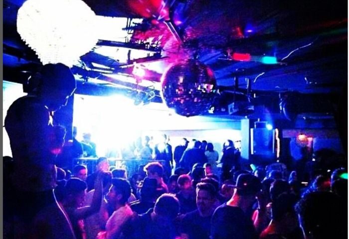 Robertson Nightclub dancefloor scene with a crowd of gay men. Disco ball and colorful lights create a vibrant atmosphere. Gay travel.