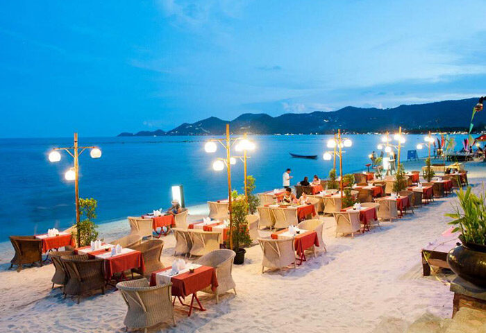 Montien House Hotel's romantic beachfront seafood restaurant at dusk. Gay hotel in Koh Samui, Thailand, with tables on the sand.