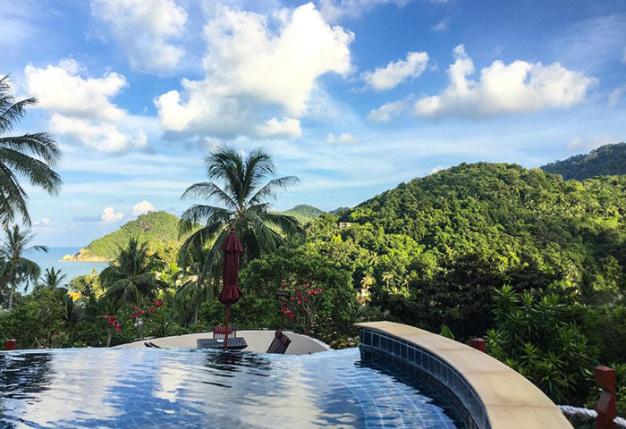 Koh Phangan Pavilions rooftop pool view. Gay hotel best deal in Thailand, with lush greenery, ocean views, and blue skies. Tropical paradise.