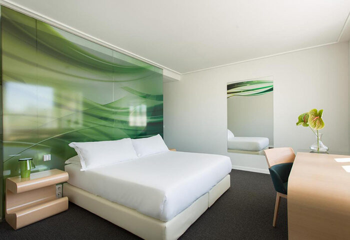 Room Mate Oscar Madrid bedroom with white linens, green accents, desk, and mirror. Best gay hotel in Chueca for this year's update.