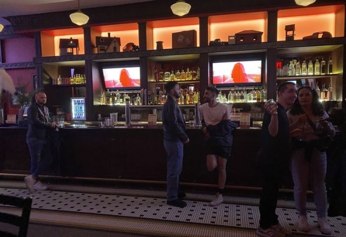 Roscoe's Tavern, a popular gay bar in Chicago. Patrons gather at the bar, with shelves of liquor and TVs in the background. Nightlife scene.