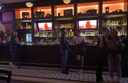 Roscoe's Tavern, a popular gay bar in Chicago. Patrons gather at the bar, with shelves of liquor and TVs in the background. Nightlife scene.