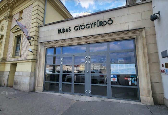 Entrance to Rudas Thermal Bath, Budapest. A popular gay-friendly spa with rooftop pool. Glass doors reflect the city. Travel advice.