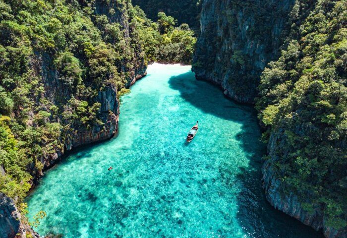 SAii Phi Phi Island Village's private beach. Gay travel destination with turquoise water, boat, and lush cliffs. Paradise found!