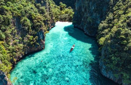 SAii Phi Phi Island Village's private beach. Gay travel destination with turquoise water, boat, and lush cliffs. Paradise found!