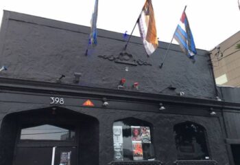 SF Eagle Bar in San Francisco. Dark building exterior with flags. A popular gay bar and leather bar in SOMA for gay men's travel.