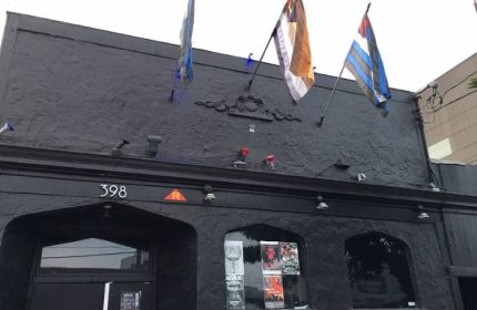 SF Eagle Bar in San Francisco. Dark building exterior with flags. A popular gay bar and leather bar in SOMA for gay men's travel.
