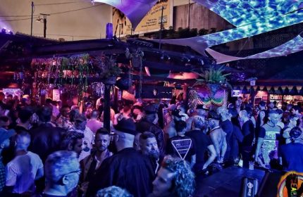 Crowded SF Eagle Bar in San Francisco. Gay bar scene with men socializing under colorful lights & canopies. Popular gay travel destination.