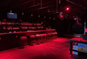 Interior of SF Eagle Bar in San Francisco. Red lighting, bar stools, bottles on the bar, and a disco ball. Gay bar travel advice.