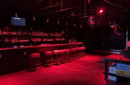 Interior of SF Eagle Bar in San Francisco. Red lighting, bar stools, bottles on the bar, and a disco ball. Gay bar travel advice.