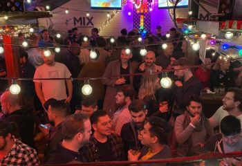 Busy night at Mix, a gay bar in San Francisco. Many men are socializing under string lights. Nightlife scene in SF.