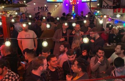 Busy night at Mix, a gay bar in San Francisco. Many men are socializing under string lights. Nightlife scene in SF.
