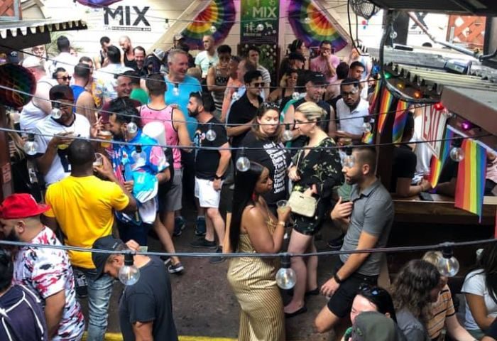 Mix Bar, a popular gay bar in San Francisco, is filled with people. Rainbow flags and string lights decorate the outdoor space. Gay travel.