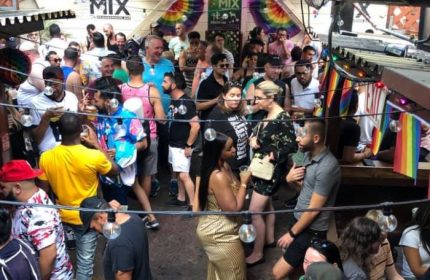 Mix Bar, a popular gay bar in San Francisco, is filled with people. Rainbow flags and string lights decorate the outdoor space. Gay travel.