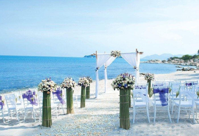 SAii Koh Samui Villas wedding setup. Beach wedding at SKS, white chairs with violet bows, floral arrangements, and a white canopy.
