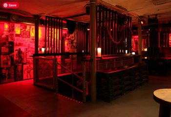 Interior of SLM Copenhagen. Red lighting, cage-like structures, posters on the wall. A gay travel destination for men, offering a unique experience.