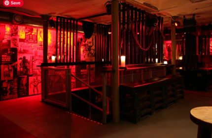 Interior of SLM Copenhagen. Red lighting, cage-like structures, posters on the wall. A gay travel destination for men, offering a unique experience.