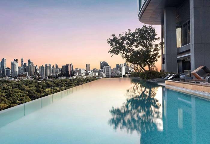 SO/ Bangkok gay hotel infinity pool with city skyline view at sunset. Modern architecture and lush greenery. Gay travel destination.