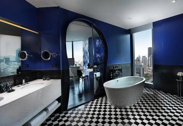 SO Sofitel Bangkok gay-friendly hotel bathroom. Blue walls, black & white checkered floor, bathtub, city view. Gay travel luxury.