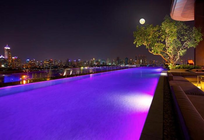 SO Sofitel Bangkok pool party at night. Gay popular rooftop pool with city skyline, full moon, and purple lighting. Gay travel.