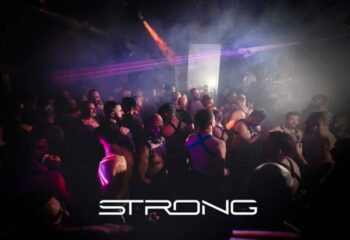 Gay cruise club STRONG in Madrid. Crowd of men in harnesses dancing in a dark, smoky club with laser lights. Gay travel nightlife.