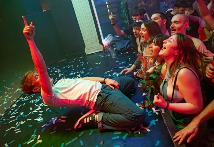 Safari Disco Club, Barcelona. Gay club scene: Man on confetti-strewn floor, arm raised, crowd cheers at this popular gay venue.