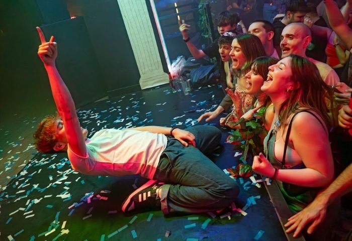 Safari Disco Club, Barcelona. Gay club scene: Man on confetti-strewn floor, arm raised, crowd cheers at this popular gay venue.