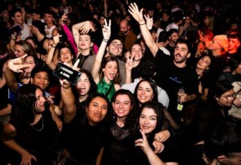 Crowd at Safari Disco Club, a gay club in Barcelona. People are smiling, posing, and holding up peace signs. One person's phone says I kissed a girl.