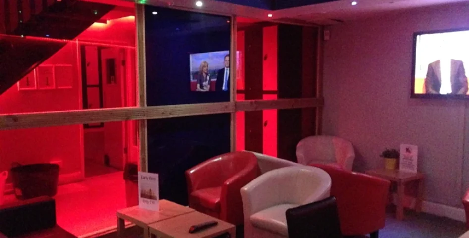 Inside Sailors Sauna, a gay sauna, with red lighting, TVs, and seating. A relaxing space for gay men to unwind and socialize.