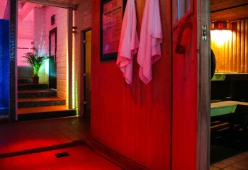 Interior of a gay sauna, sailors sauna, with red walls, towels, a shower room with blue lighting, and a traditional sauna room.