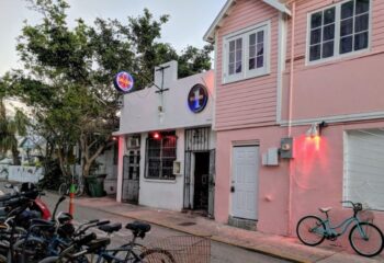 Saloon 1, a Key West gay bar in Florida. The bar's entrance is visible, with bikes parked nearby. Pink building next door.